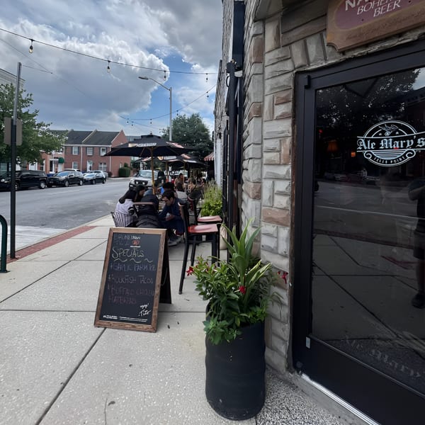 Ale Mary's restaurant exterior with people dining at outdoor tables under umbrellas on a cloudy day.