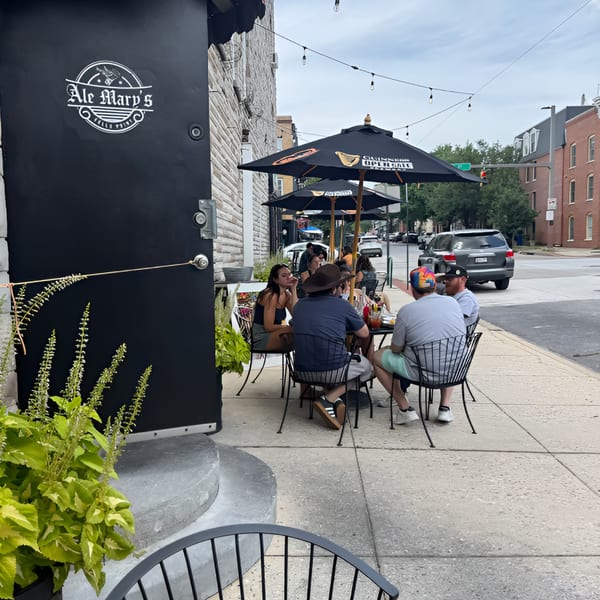 Patrons enjoying outdoor dining at Ale Mary's, with black umbrellas and string lights on a city sidewalk.