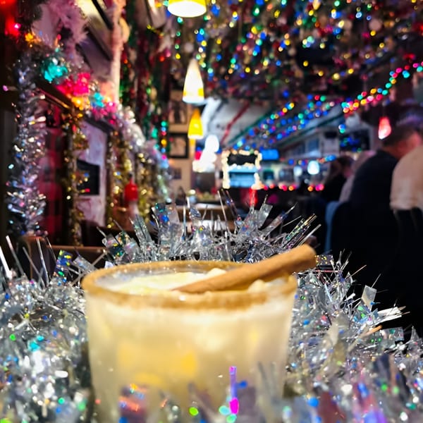 A festive Ale Mary's bar with a drink and tinsel in the foreground, colorful lights in the background.
