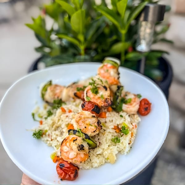 Grilled shrimp and vegetable skewers over rice pilaf with parsley on a white plate.