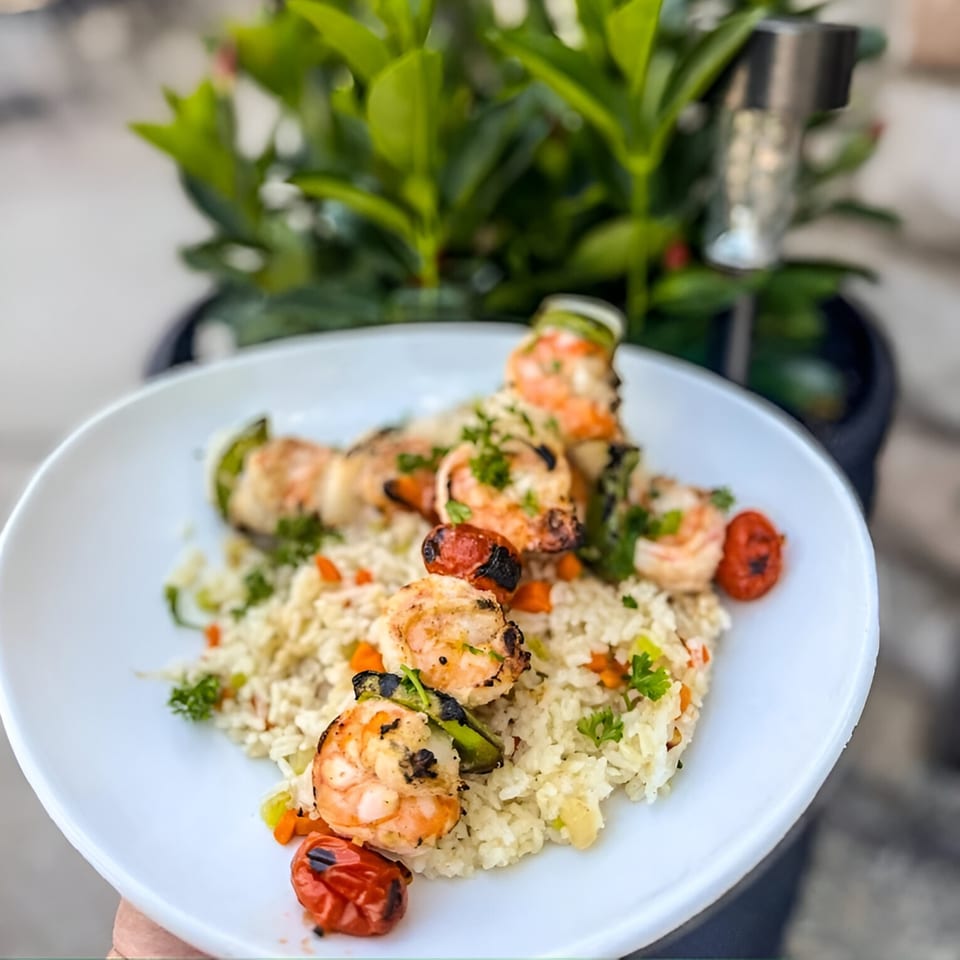 Grilled shrimp and vegetable skewers over rice pilaf with parsley on a white plate.