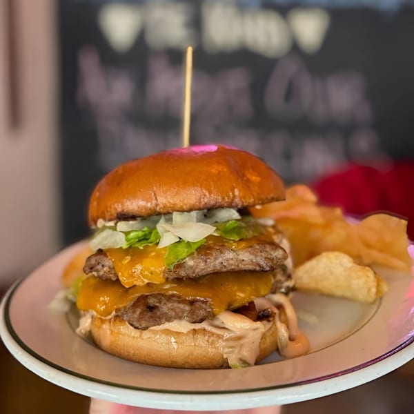 A double cheeseburger with lettuce, onions, and sauce, served with potato chips on a white plate.