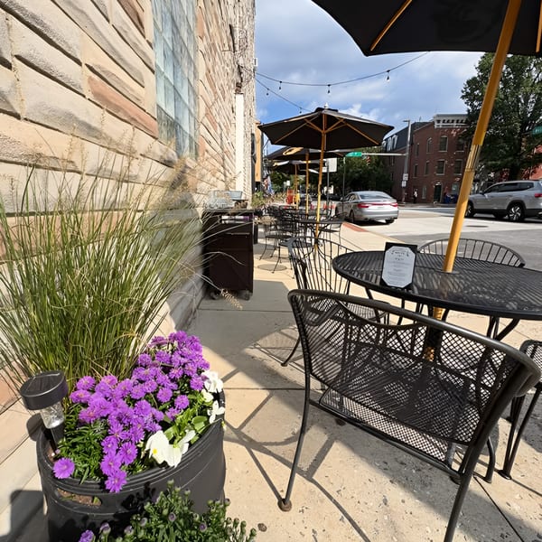 Ale Mary's outdoor patio with black tables, chairs, umbrellas, and purple flowers in planters.