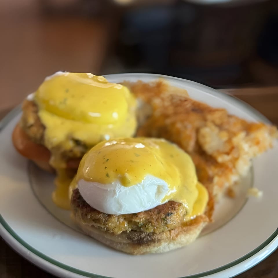 Two eggs benedict with hollandaise sauce and hash browns on a white plate at Ale Mary's.