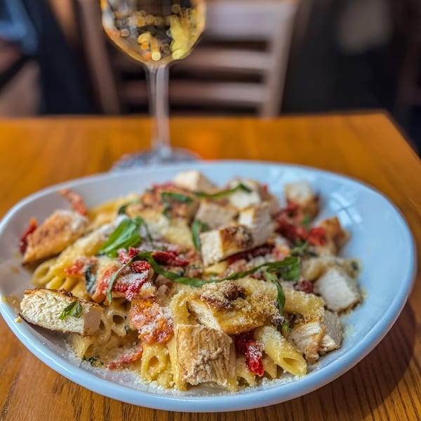 Ale Mary's chicken penne pasta with sun-dried tomatoes, basil, and parmesan cheese, with a glass of white wine.